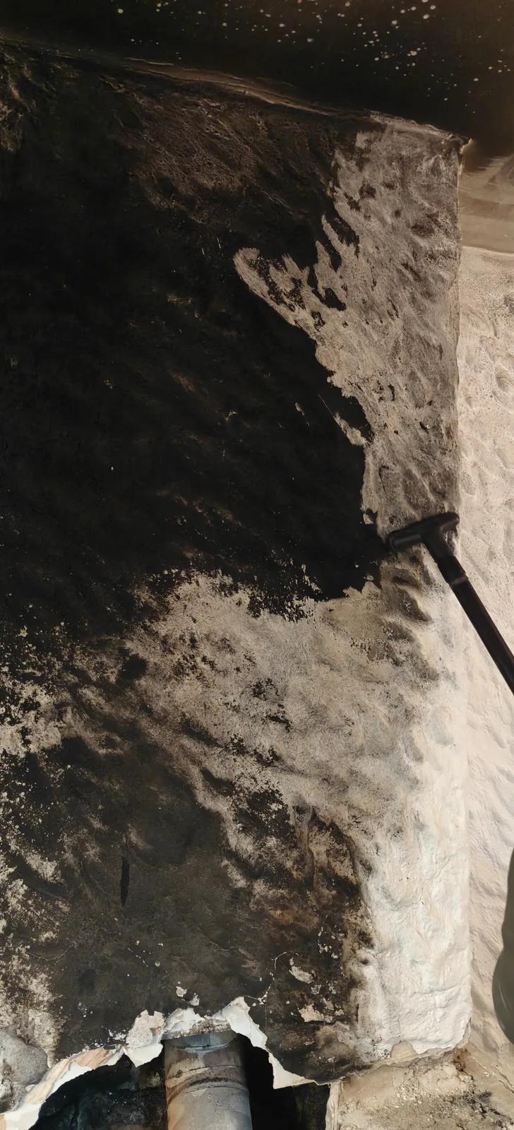 Limpieza despues de incendio: pared de piedra natural cubierta de hollín durante el proceso de descontaminación profesional. A la derecha la zona ya tratada, a la izquierda todavía con la capa de carbón ácido por retirar.
